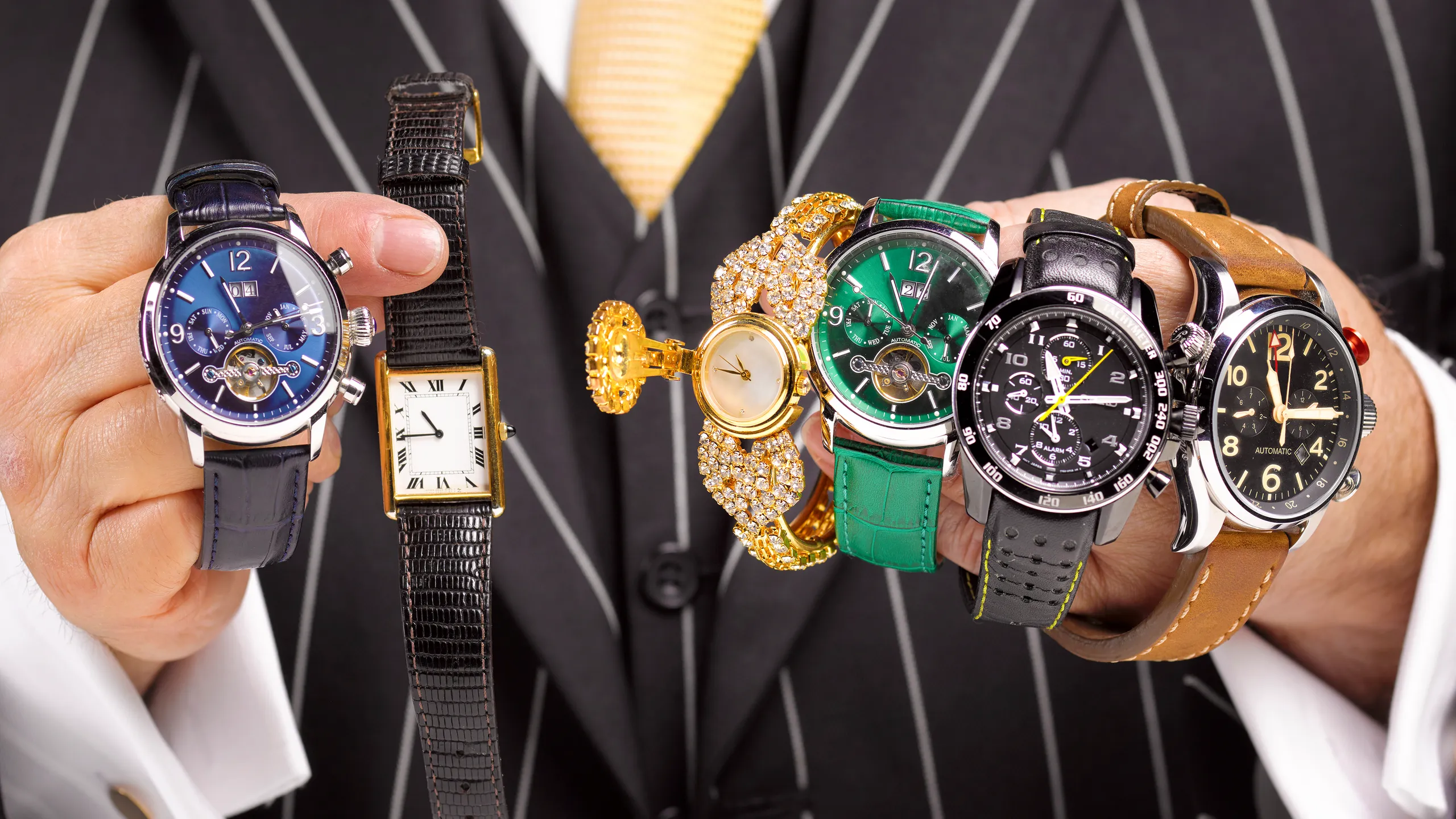 hombre con traje sosteniendo varios relojes de marcas de lujo