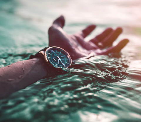 mano de un hombre sumergiendo el reloj sobre el agua